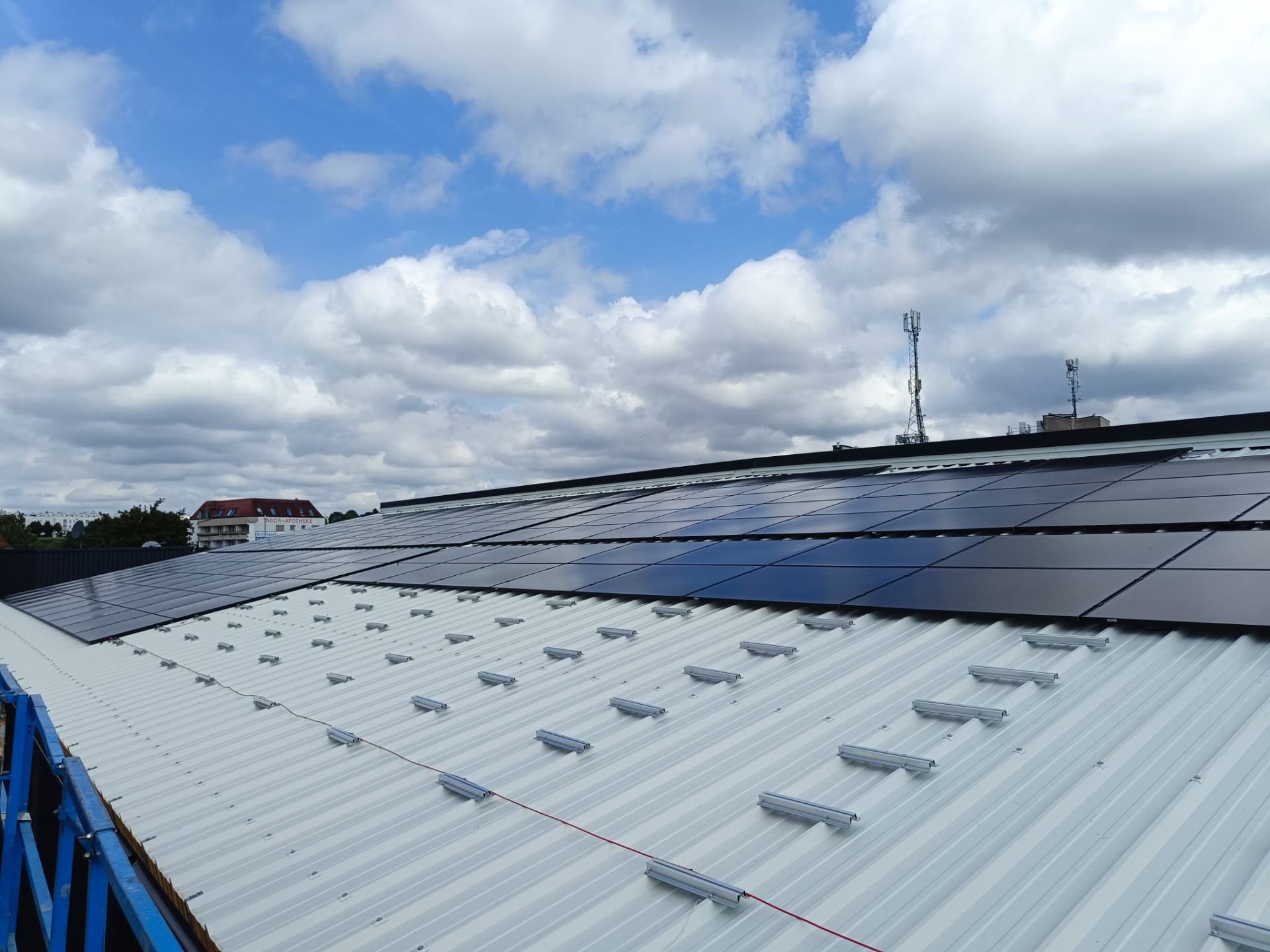 Photovoltaik-Anlage auf einem Trapezblech-Hallendach mit Aluminium-Unterkonstruktion und schwarzen Full-Black-Modulen unter blauem Wolkenhimmel